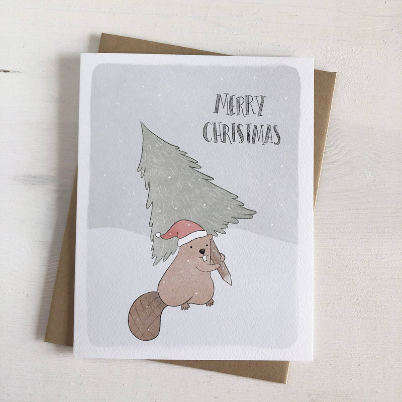 A card featuring an illustration of a beaver wearing a Santa hat and carrying a Christmas tree in falling snow. 